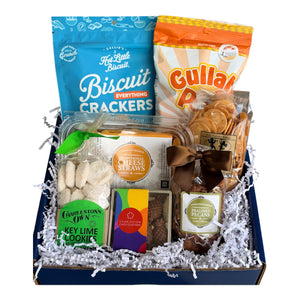 Holy City Snack Sampler with Callie's Hot Little Biscuit Everything Biscuit Crackers, Lillie's of Charleston "Ho Lotta Hissy Fit" Gullah Pop, Olde Colony Bakery Benne Wafers, Charleston Favorites Cheese Straws, Charleston Chocolatiers "Hospitality Pineapple" Chocolate Box, and Charleston Favorites Praline Pecans packed in a branded blue Essentially Charleston gift box.